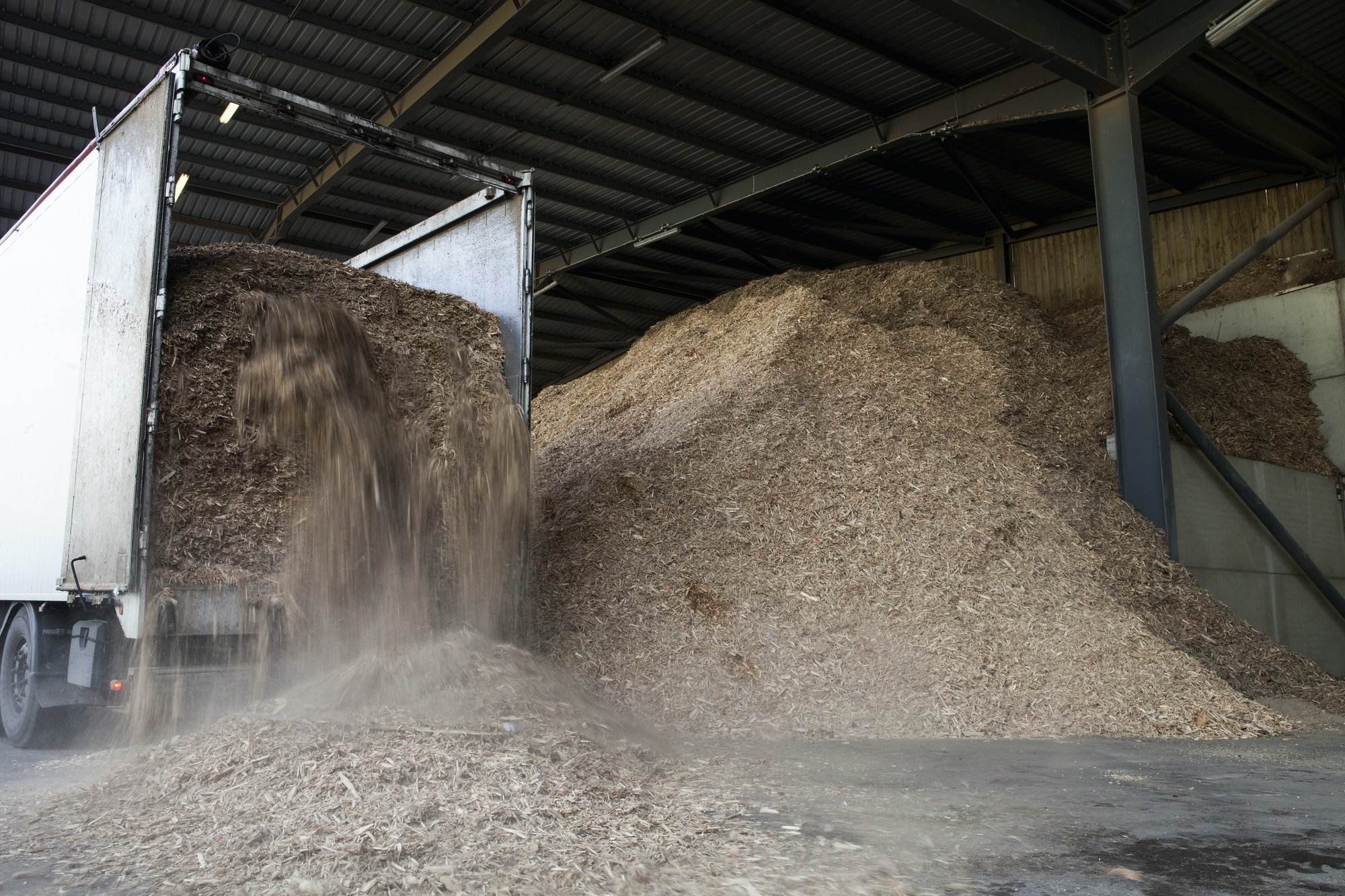 Stored organic waste being poured from a lorry into a large warehouse for biomass fuel production.